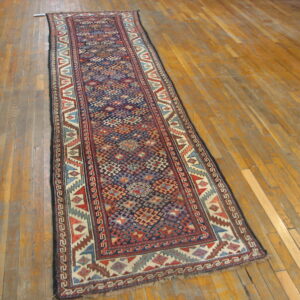Low-pile runner rug with a dense navy and red geometric pattern resting on worn hardwood flooring.