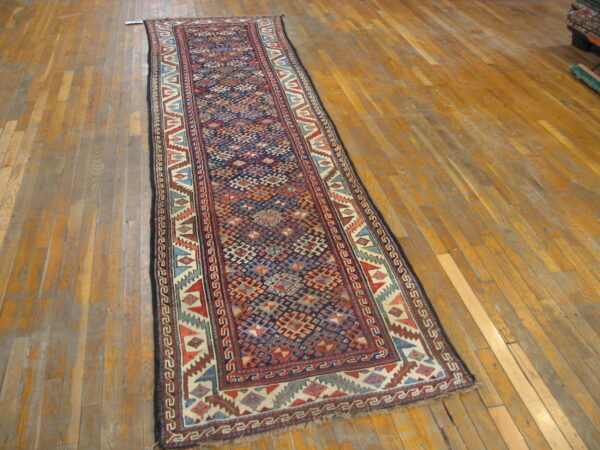 Low-pile runner rug with a dense navy and red geometric pattern resting on worn hardwood flooring.