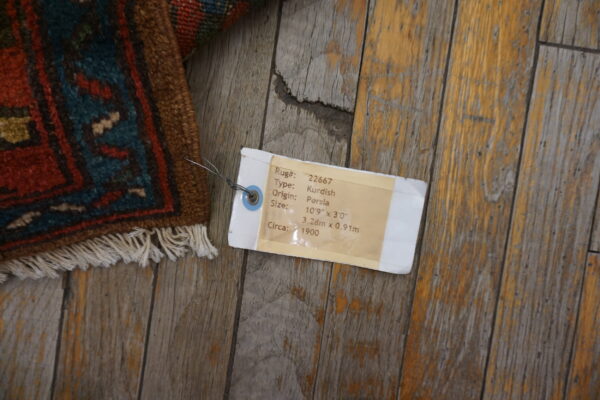 A corner of a low-pile rug featuring red and teal geometric patterns rests on distressed wood planks.