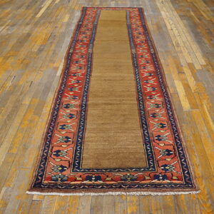 A camel runner rug with red, navy, and tan patterned borders rests on wide, distressed wooden floor planks.