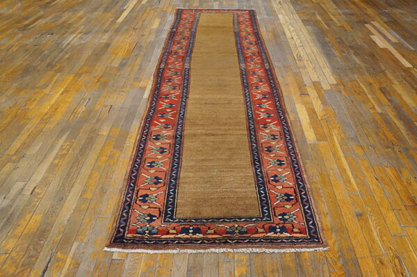 A camel runner rug with red, navy, and tan patterned borders rests on wide, distressed wooden floor planks.