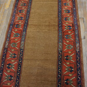 Low-pile brown runner with patterned red and blue floral borders rests on distressed wooden planks.