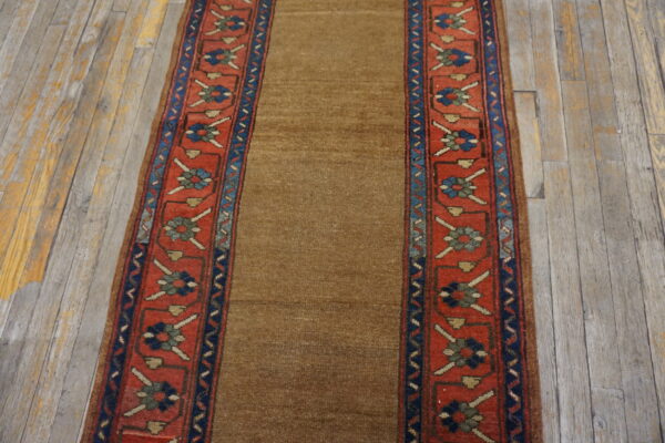 Low-pile brown runner with patterned red and blue floral borders rests on distressed wooden planks.