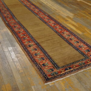 Low-pile runner in solid tan with red and navy patterned borders displayed on rustic wood flooring.
