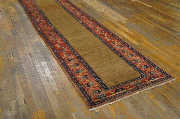 Low-pile runner in solid tan with red and navy patterned borders displayed on rustic wood flooring.