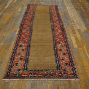Narrow runner rug with a solid brown field and a detailed red and navy blue border on distressed wood.