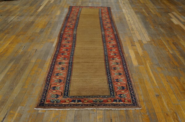 Narrow runner rug with a solid brown field and a detailed red and navy blue border on distressed wood.