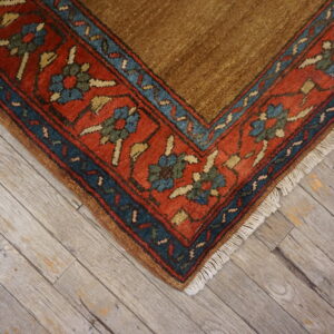 Brown rug corner featuring a rust red, blue, and green patterned border resting on weathered wood planks.