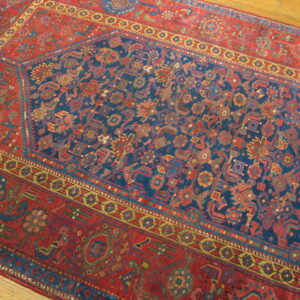 Close-up of a low-pile rug featuring a navy geometric field and detailed red borders on hardwood flooring.