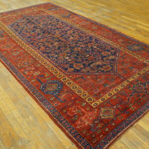 A large red and navy traditional rug with intricate geometric patterns rests on wide plank hardwood flooring.