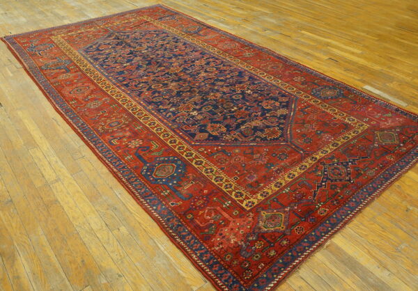 A large red and navy traditional rug with intricate geometric patterns rests on wide plank hardwood flooring.