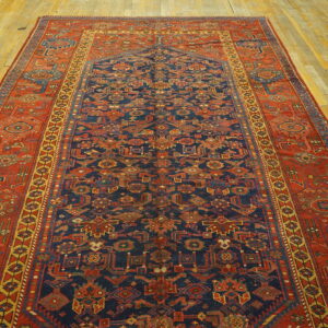 Geometric rug featuring a navy blue field and wide rust-red border, placed on light wooden plank flooring.