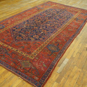 Low-pile rug featuring a navy geometric central panel and wide rust-red border on distressed light wood floors.