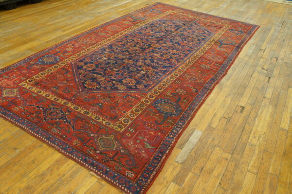 Low-pile rug featuring a navy geometric central panel and wide rust-red border on distressed light wood floors.