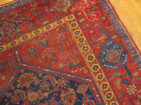 Red, blue, and gold geometric rug with a detailed border rests on light hardwood flooring.