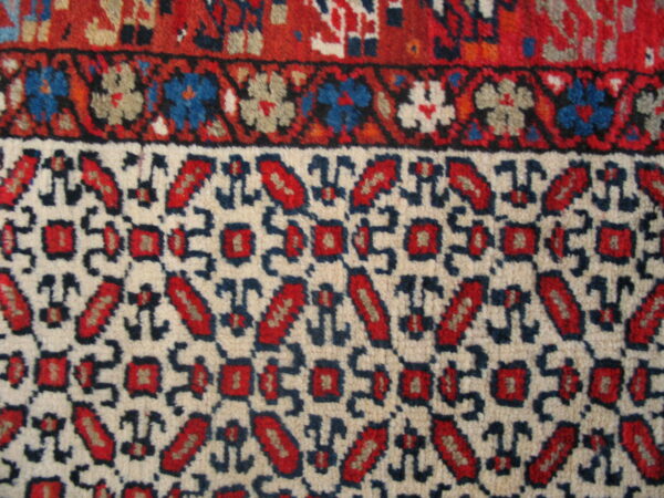 Rug detail showing red, cream, and dark blue geometric borders with stylized floral and repeating motifs.