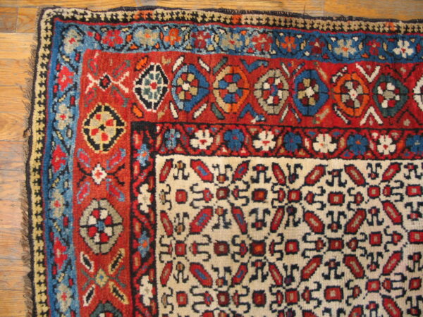 Red, blue, and cream geometric patterned rug showing corner details and fringes on wood flooring.