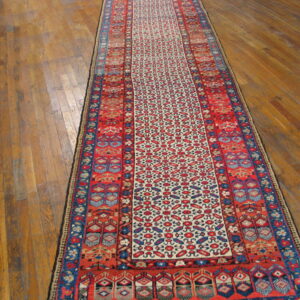 Red, blue, and cream geometric runner rug displayed lengthwise on distressed wood plank flooring.