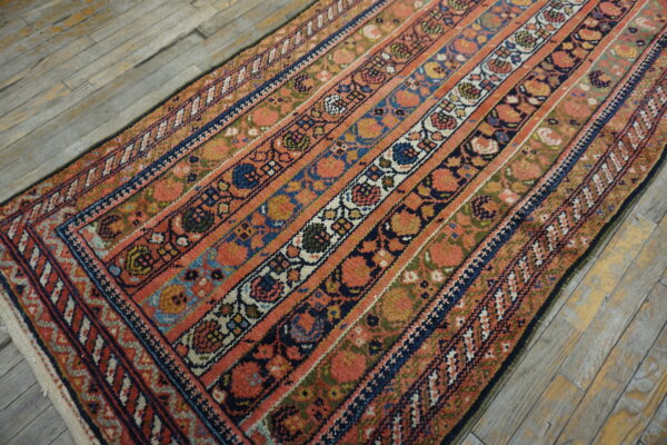 A runner rug with bands of coral, navy, and green floral patterns rests on weathered wood floors.