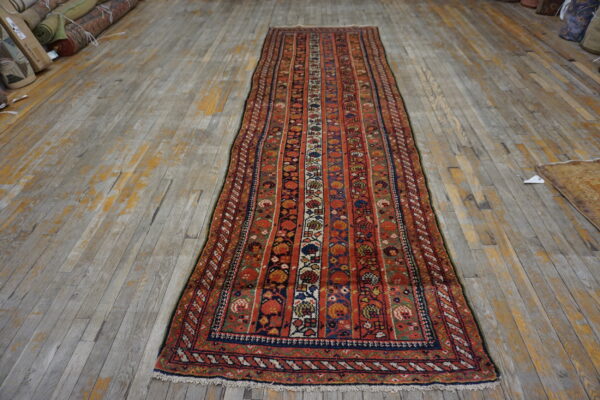 Red and blue runner rug with striped floral motifs displayed on distressed gray wood planks.