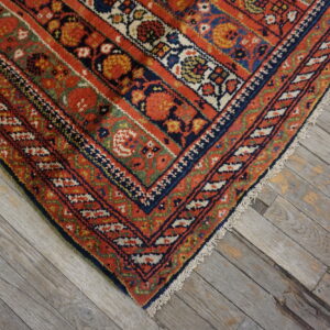 Ornate red and blue patterned rug corner with fringes resting on weathered gray hardwood flooring.