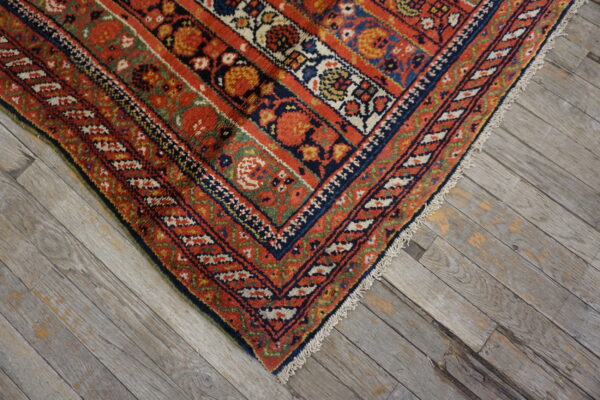Ornate red and blue patterned rug corner with fringes resting on weathered gray hardwood flooring.