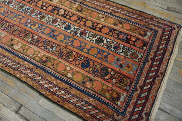 Low-pile rug featuring detailed coral, navy, and earth-toned striped bands on gray wooden flooring.
