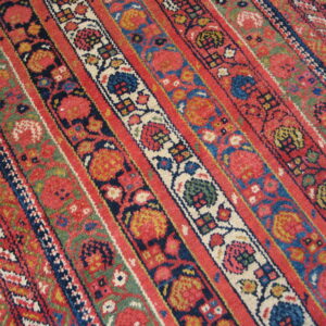 Low-pile rug with colorful red, blue, green, and cream floral and geometric striped patterns.