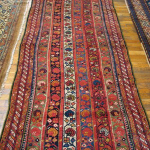 Multicolored runner rug featuring vertical panels of red, blue, green, and ivory geometric designs on wood floor.