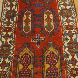 Red runner rug featuring traditional geometric designs in blue, gold, and cream on light wood plank flooring.
