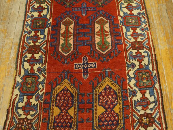 Red runner rug featuring traditional geometric designs in blue, gold, and cream on light wood plank flooring.