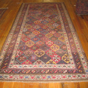 A colorful geometric diamond pattern rug with wide borders lays on polished wooden floorboards.
