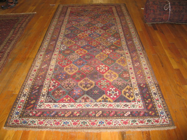 A colorful geometric diamond pattern rug with wide borders lays on polished wooden floorboards.