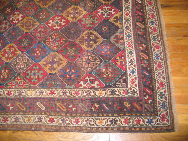 Multi-colored geometric rug with alternating diamond shapes and a complex floral border on wood flooring.