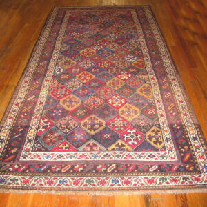 A large multi-colored geometric rug with diamond medallions and patterned borders lies on wood planks.