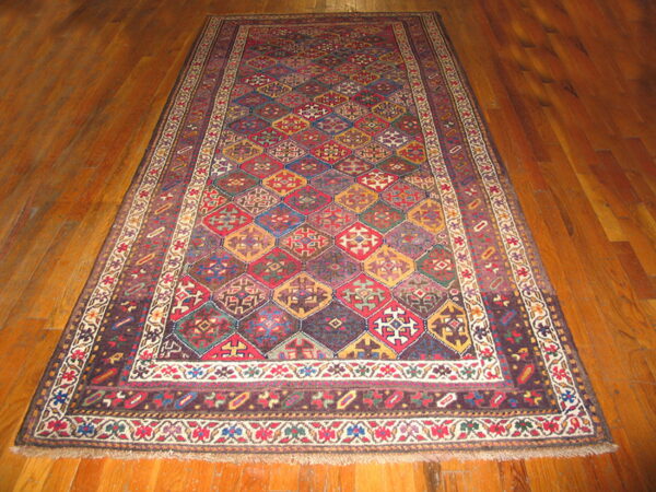 A large multi-colored geometric rug with diamond medallions and patterned borders lies on wood planks.