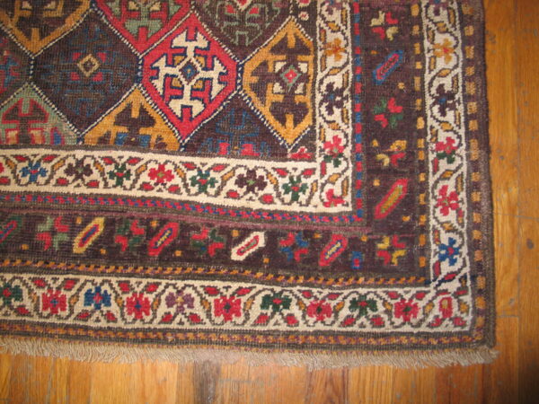 Low-pile rug corner showing dark brown geometric field and detailed floral borders on light brown hardwood.