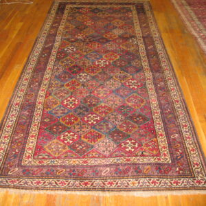 A long, dark runner rug with a repeating geometric multicolored diamond pattern rests on hardwood floor.