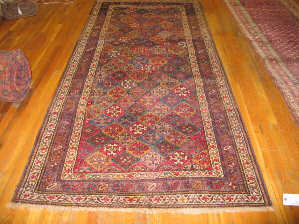 A long, dark runner rug with a repeating geometric multicolored diamond pattern rests on hardwood floor.