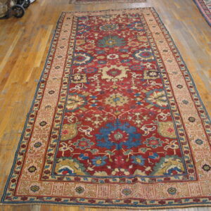 Traditional red runner rug featuring intricate blue and cream floral motifs lies on worn wooden flooring.
