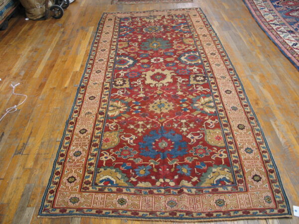 Traditional red runner rug featuring intricate blue and cream floral motifs lies on worn wooden flooring.