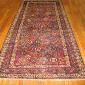 Geometric rug with complex red, gold, and blue diamond patterns lying on shiny wood planks.