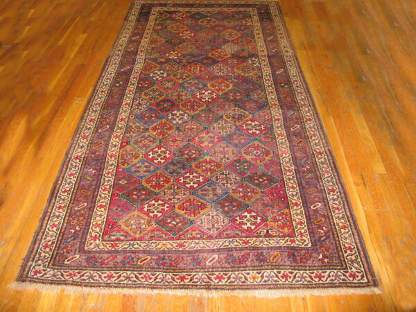 Geometric rug with complex red, gold, and blue diamond patterns lying on shiny wood planks.