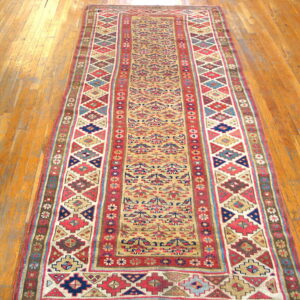 Geometric runner rug with tan field and complex red and blue borders on wooden flooring.