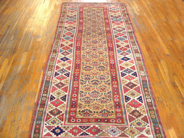 Geometric runner rug with tan field and complex red and blue borders on wooden flooring.