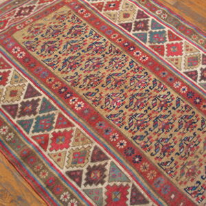 Muted red, tan, blue, and brown geometric pattern runner rug laid over wide wood planks.