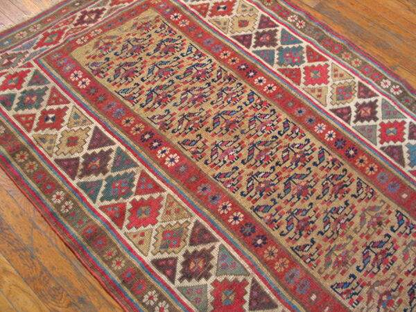 Muted red, tan, blue, and brown geometric pattern runner rug laid over wide wood planks.