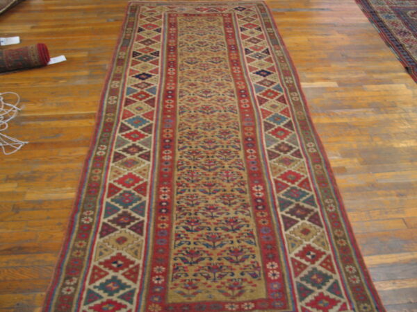 A colorful runner rug features a tan floral field and borders with red, blue, and brown geometric motifs.