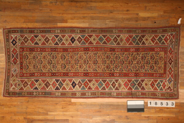 Red and tan geometric runner rug featuring repeating diamonds and a patterned central field on wooden planks.