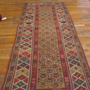 Tan, red, and blue runner rug featuring stylized floral motifs and geometric borders on light wood flooring.